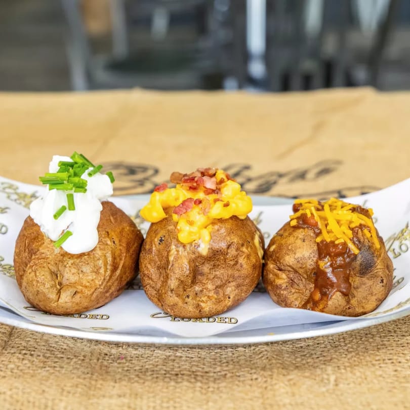 Three Baked and Loaded potatoes with different toppings: sour cream and chives, mac and cheese with bacon, and chili with shredded cheese.