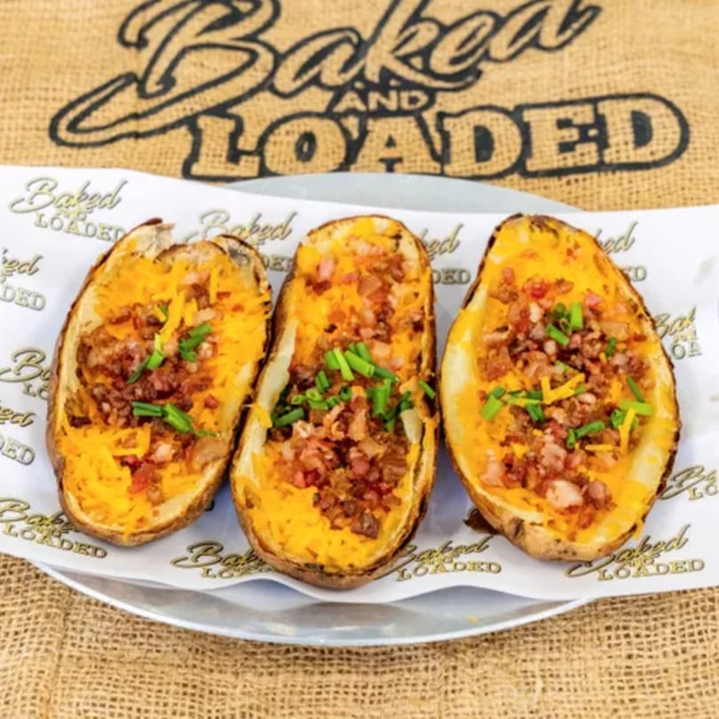 Three Baked and Loaded potato skins filled with cheese, bacon bits, and chives on a white plate.