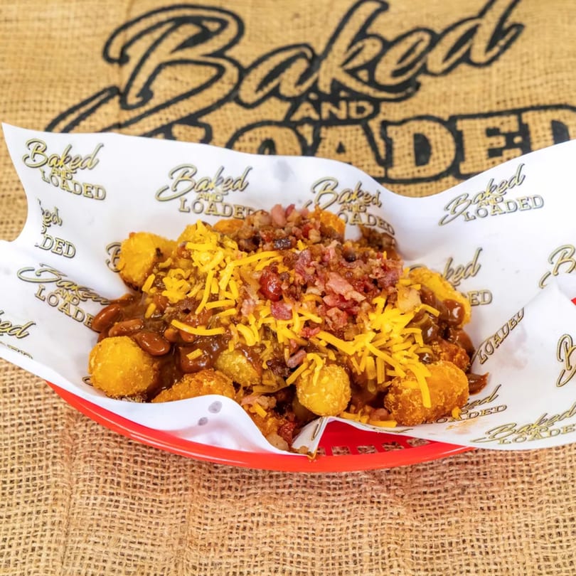 Chili cheese tater tots with bacon bits in a red basket, on a burlap background.