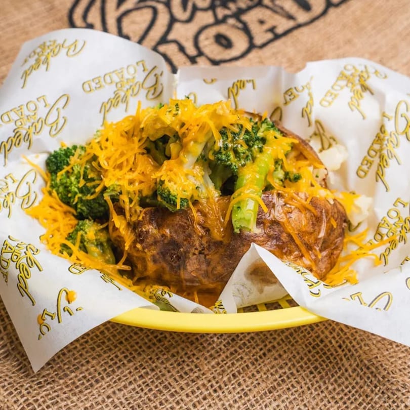 Baked potato loaded with broccoli and melted cheddar cheese in a yellow basket with "Baked and Loaded" paper.