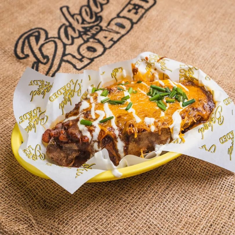 A Baked and Loaded chili cheese baked potato with sour cream and chives in a yellow basket.